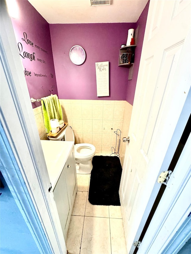 bathroom with visible vents, toilet, tile patterned flooring, vanity, and tile walls