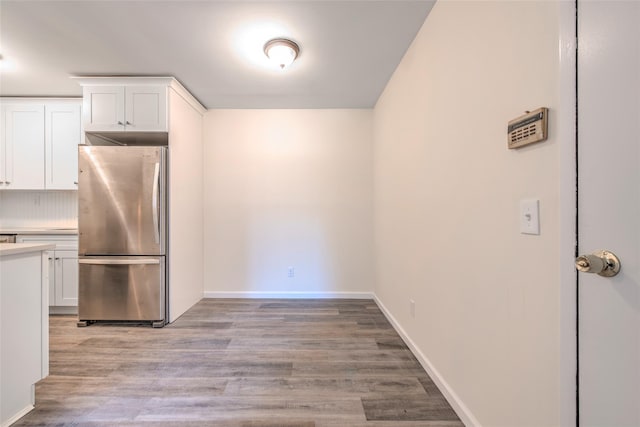 kitchen featuring light wood finished floors, baseboards, freestanding refrigerator, light countertops, and white cabinetry