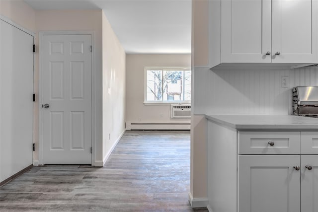 kitchen featuring white cabinets, light wood-style flooring, baseboard heating, light countertops, and a wall mounted AC