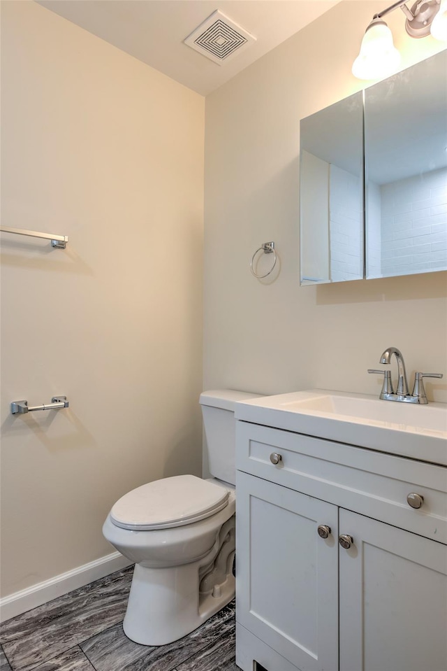 half bath with visible vents, toilet, vanity, wood finished floors, and baseboards