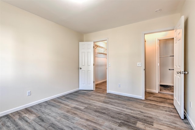 unfurnished bedroom with a spacious closet, baseboards, and wood finished floors