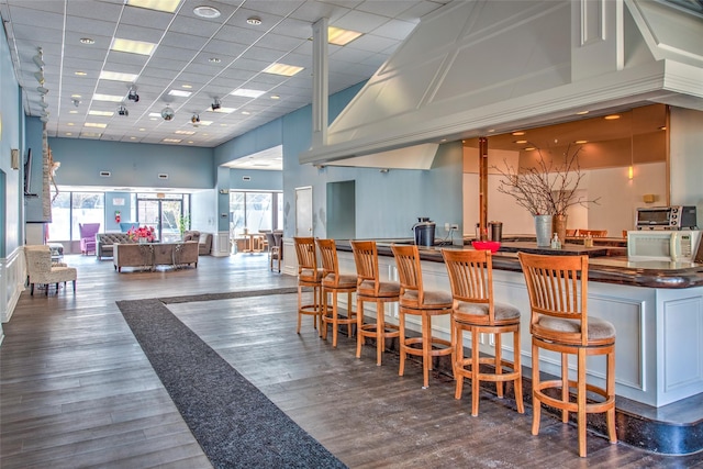 bar with a high ceiling, a drop ceiling, wood finished floors, and a community bar