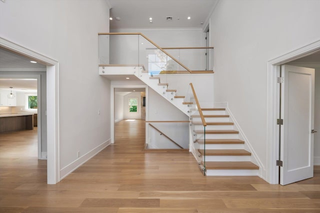 stairs featuring ornamental molding, a high ceiling, wood finished floors, and a healthy amount of sunlight