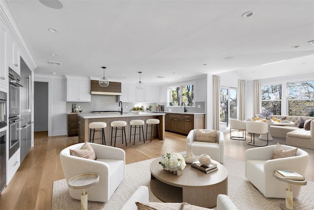 living room with recessed lighting, visible vents, baseboards, light wood finished floors, and crown molding