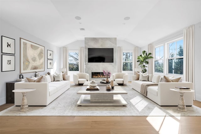 living area with a fireplace, visible vents, vaulted ceiling, and wood finished floors