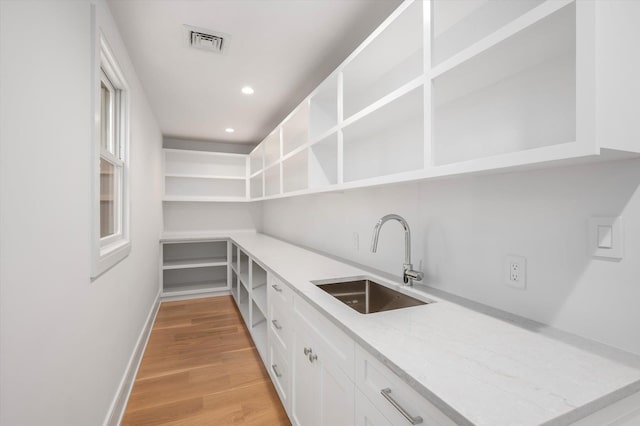 interior space featuring open shelves, visible vents, light wood-style floors, white cabinetry, and a sink