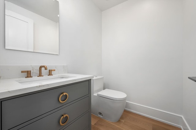 half bathroom with baseboards, decorative backsplash, toilet, wood finished floors, and vanity