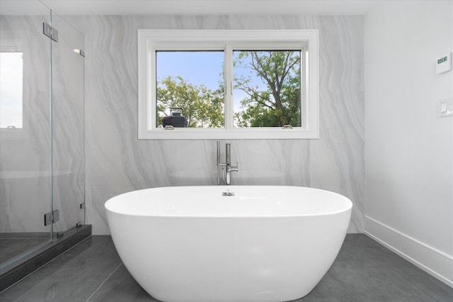 full bath with a freestanding tub, a healthy amount of sunlight, baseboards, and a marble finish shower