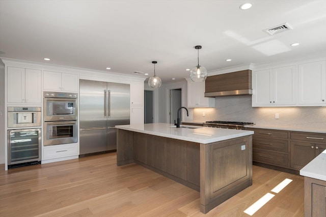 kitchen featuring wine cooler, custom exhaust hood, light countertops, appliances with stainless steel finishes, and a sink