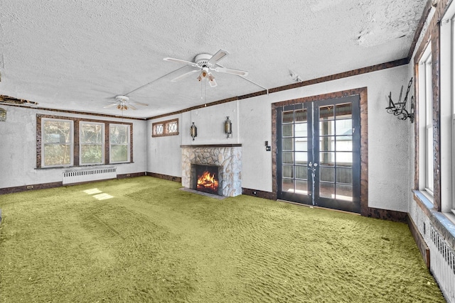 unfurnished living room with carpet floors, a textured wall, radiator, a stone fireplace, and a healthy amount of sunlight