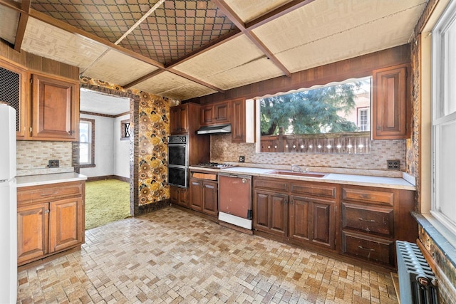 kitchen with dishwashing machine, under cabinet range hood, a sink, light countertops, and radiator