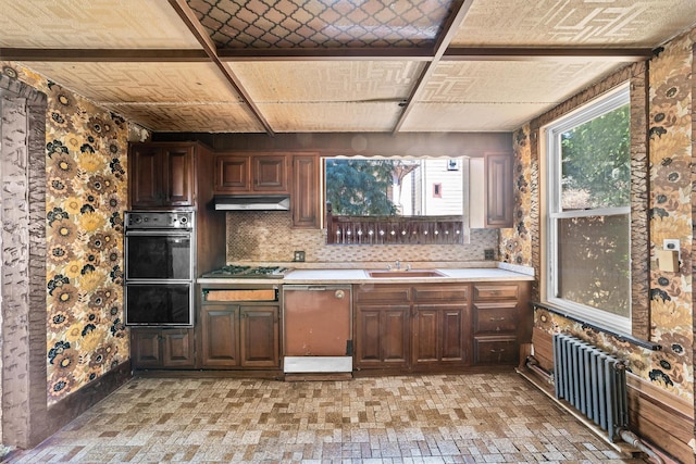 kitchen with radiator, oven, light countertops, under cabinet range hood, and a warming drawer