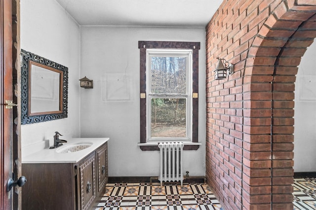 bathroom with brick wall, radiator heating unit, vanity, and tile patterned floors