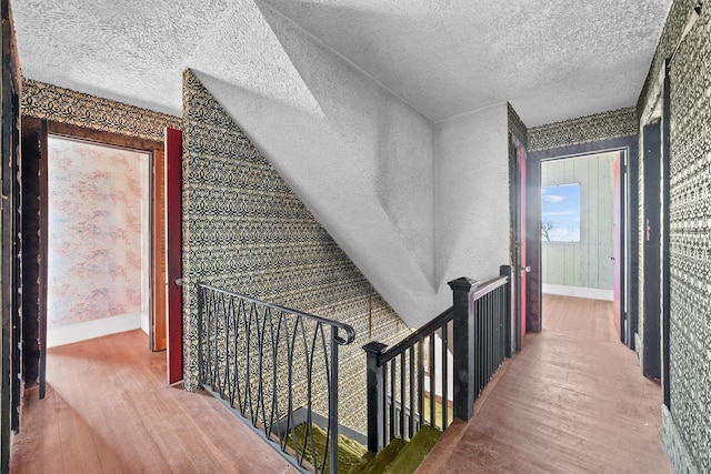 hallway with a textured ceiling, baseboards, and wood finished floors