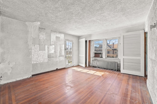 empty room with a textured ceiling, radiator heating unit, and hardwood / wood-style flooring