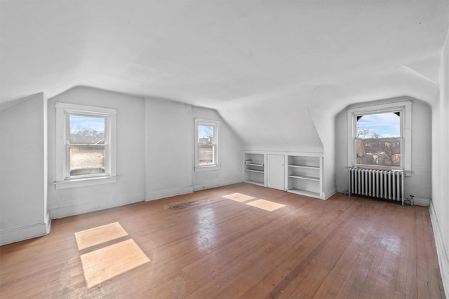 additional living space with built in shelves, radiator heating unit, wood-type flooring, and a wealth of natural light