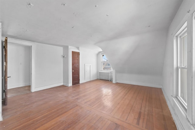 bonus room featuring vaulted ceiling, radiator heating unit, wood-type flooring, and baseboards