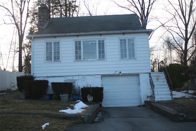 view of front facade featuring aphalt driveway, a garage, fence, roof with shingles, and a chimney