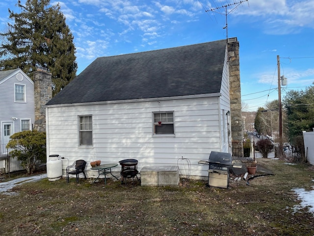 rear view of property featuring a chimney and roof with shingles