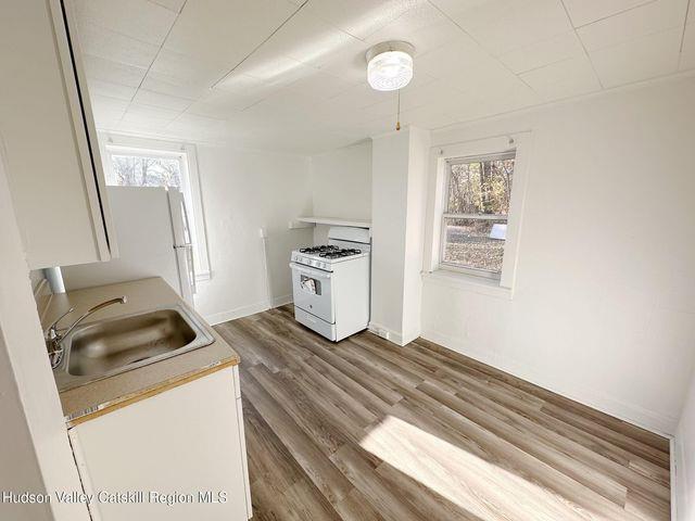 kitchen featuring light countertops, a sink, wood finished floors, white appliances, and baseboards
