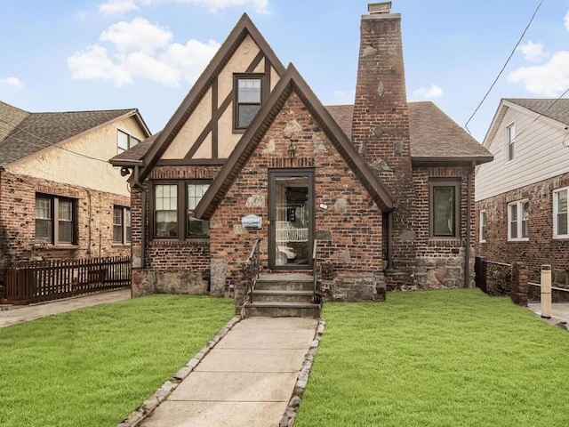 tudor house with brick siding, roof with shingles, stucco siding, a chimney, and a front yard