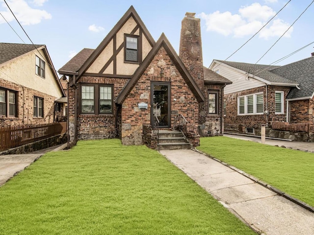 tudor-style house with brick siding, a chimney, stucco siding, a front yard, and fence