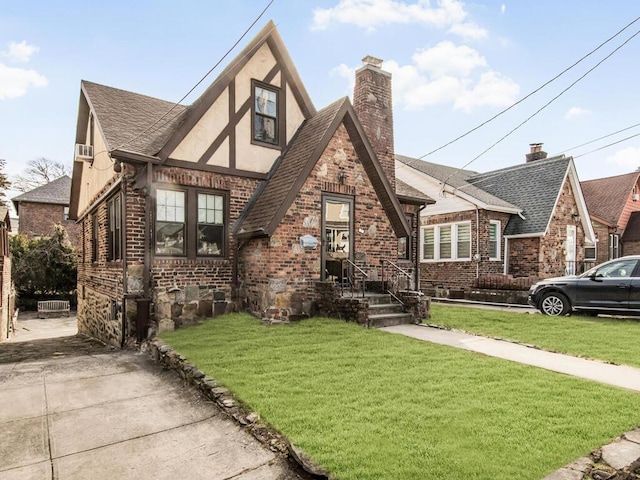 tudor home featuring brick siding, roof with shingles, a chimney, stucco siding, and a front lawn