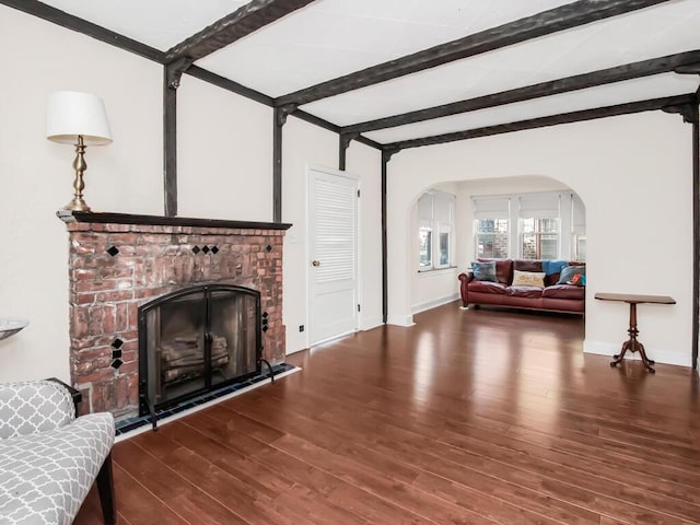 living area featuring arched walkways, dark wood-style flooring, beam ceiling, and baseboards