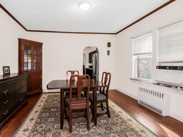 dining room with arched walkways, ornamental molding, radiator heating unit, and dark wood finished floors