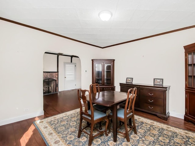 dining area featuring arched walkways, a fireplace, dark wood-style floors, and baseboards