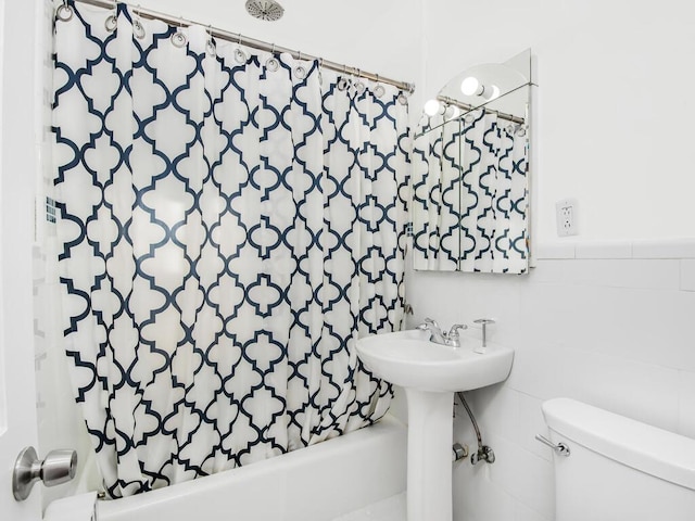 full bathroom with tile walls, wainscoting, shower / bathtub combination with curtain, and toilet