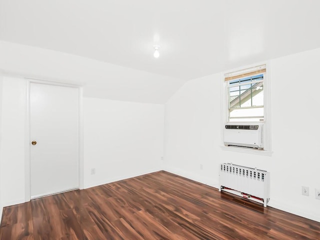 additional living space featuring vaulted ceiling, dark wood-style flooring, radiator heating unit, and cooling unit