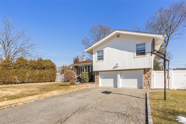 tri-level home with aphalt driveway, a garage, fence, stone siding, and a gate