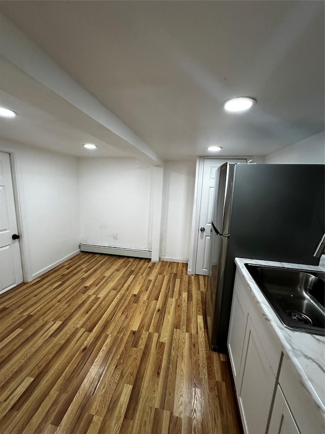 kitchen with a baseboard radiator, wood finished floors, a sink, light countertops, and freestanding refrigerator