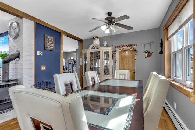 dining area with a wood stove, a baseboard radiator, ceiling fan, and wood finished floors