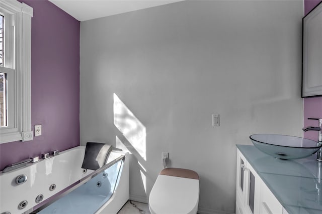 bathroom with marble finish floor, toilet, vanity, and a whirlpool tub