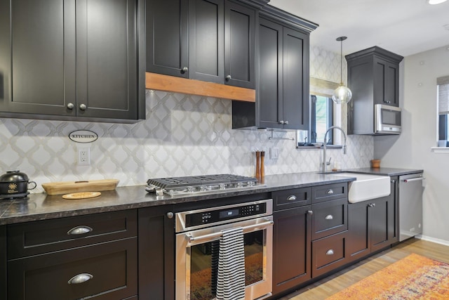 kitchen with decorative backsplash, appliances with stainless steel finishes, light wood-type flooring, pendant lighting, and a sink