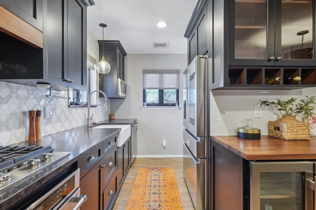 kitchen featuring wine cooler, a sink, visible vents, appliances with stainless steel finishes, and glass insert cabinets