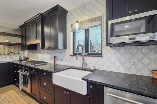 kitchen featuring decorative backsplash, appliances with stainless steel finishes, light wood-type flooring, pendant lighting, and a sink