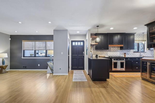 kitchen featuring baseboards, appliances with stainless steel finishes, dark cabinetry, light wood-style floors, and backsplash