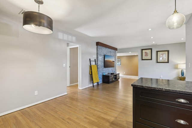 kitchen featuring hanging light fixtures, dark countertops, light wood-style flooring, and baseboards