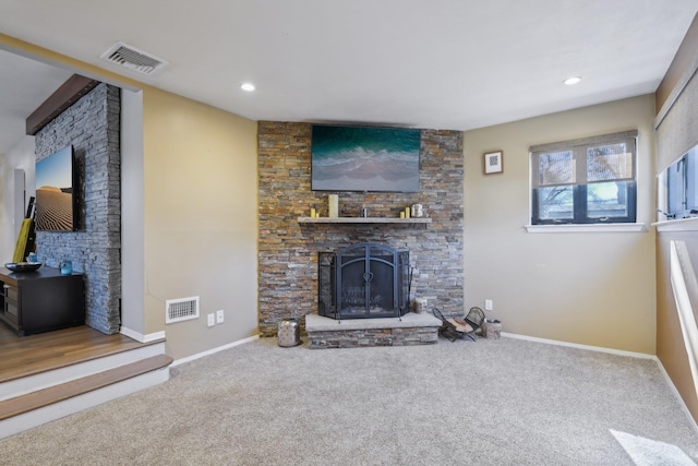 living room featuring a stone fireplace, carpet, visible vents, and baseboards