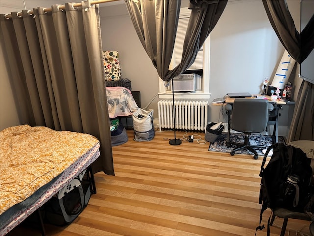 bedroom with cooling unit, wood finished floors, and radiator