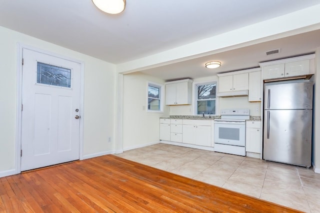 kitchen with white electric stove, visible vents, freestanding refrigerator, light countertops, and under cabinet range hood