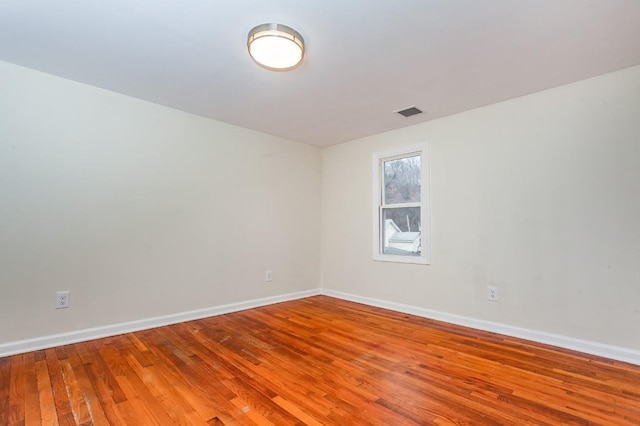 unfurnished room featuring baseboards, visible vents, and hardwood / wood-style floors