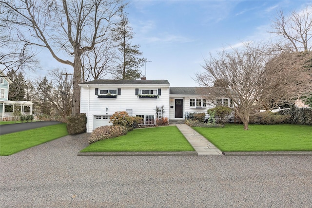 split level home with an attached garage, a front lawn, a chimney, and gravel driveway