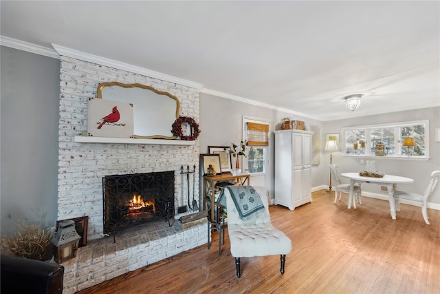 living area with light wood-style flooring, a fireplace, ornamental molding, and baseboards