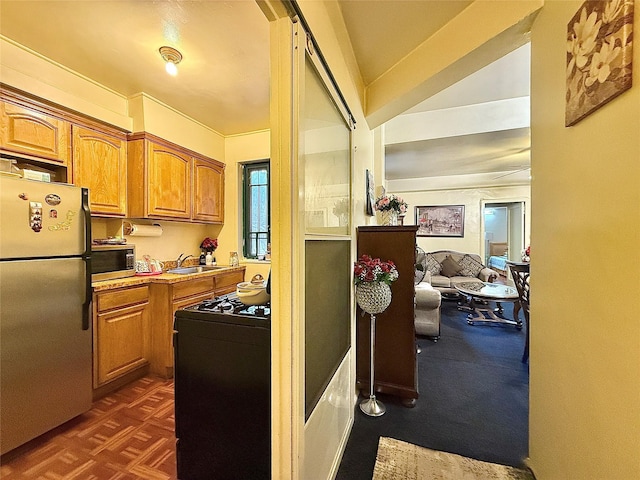 kitchen featuring range with gas stovetop, stainless steel microwave, brown cabinets, freestanding refrigerator, and a sink