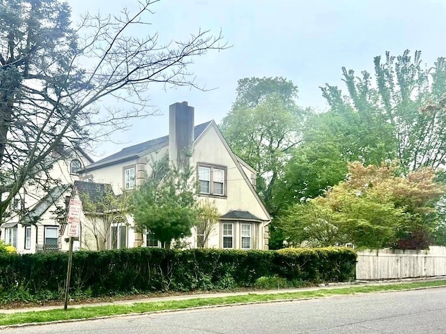 view of property exterior with a chimney, fence, and stucco siding