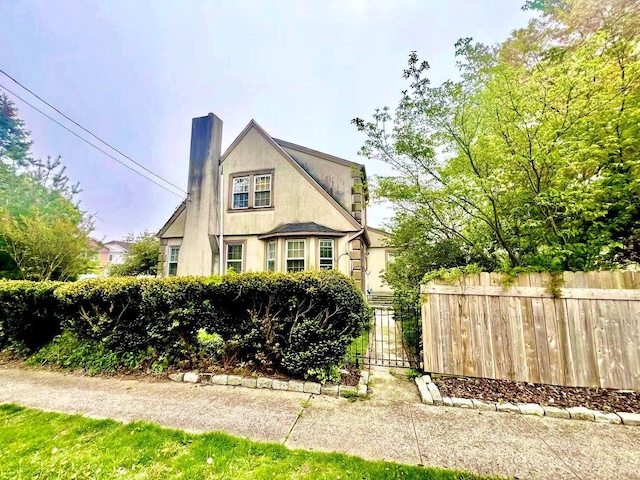 view of front facade featuring fence, a chimney, and stucco siding